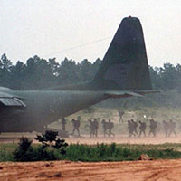 Soldiers from Company A, 112th Signal Battalion conduct an engine running operation (i.e. ‘hot load’) onto a waiting C-130 Hercules aircraft in preparation for an airborne operation at Sicily Drop Zone, Fort Bragg, NC in March 1990. The Airborne requirement helped build esprit de corps and promoted an elite mindset among 112th soldiers. <i>(Photo courtesy of James S. Kestner)</i>