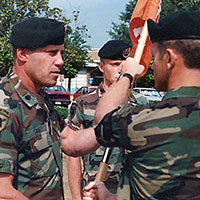 CPT Steve Kestner (right) hands off the Company A, 112th Signal Battalion guidon to his battalion commander, LTC Steven R. Sawdey, at a June 1990 change-of-command ceremony. Incoming commander, CPT Eric G. David (center), stands ready to receive it. Kestner, David, and Sawdey all deployed to Panama during Operation JUST CAUSE. (Photo courtesy of James S. Kestner)