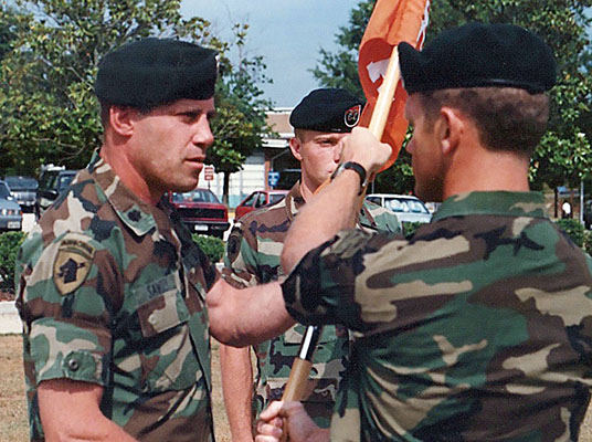 CPT Steve Kestner hands off the Company A, 112th Signal Battalion guidon to his battalion commander, LTC Steven R. Sawdey, at a June 1990 change-of-command ceremony. Incoming commander, CPT Eric G. David, stands ready to receive it.