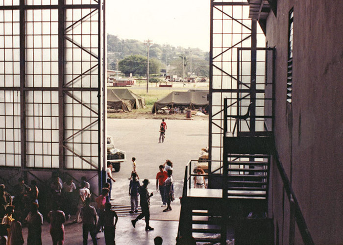 Displaced civilians are shown to their housing cubicles on 13 January 1990. Through the open hangar door are some of the GP Medium tents used to house single males.