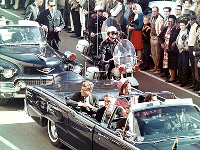 With Texas Governor John Connally seated directly in front of him, President Kennedy smiles at an adoring crowd just minutes before his assassination in Dealey Plaza
