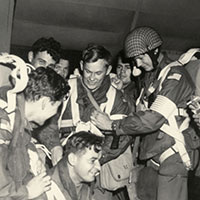 OG ADRIAN utilized numerous pieces of British equipment, including parachutes, helmets, and Dennison jump smocks. 