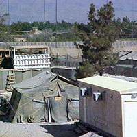 View of temporary guard towers constructed atop a HESCO wall.  HESCOs filled with dirt and gravel were used for perimeter and interior walls.  They were replaced in later years by concrete T-walls (large concrete forms in the shape of inverted ‘T’s). The advantages of HESCOs are that they can be easily sited and filled, and provide excellent protection from direct-fire weapons and improvised explosive devices (IEDs).