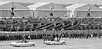 A battery of truck-mounted MGR-1 <i>Honest John</i> surface-to-surface nuclear-capable rockets can be seen behind the soldiers.