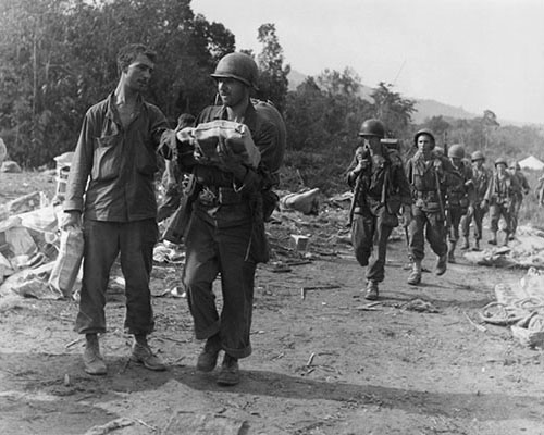 This 29 April 1944 photograph shows the Marauders of Khaki Combat Team picking up a three-day supply of ‘K’ rations as they set out on yet another leg of their march through Burma. The daily K ration, divided into three meals, contained three thousand calories compressed into the most compact form possible. Ration staples included the four ounce U.S. Army field ration D (a dense bar consisting of chocolate, skim milk powder, sugar, oat flour, cocoa fat, vitamins C and B, and artificial flavoring), a small can of chopped ham and egg or a can of processed cheese, a K-1 biscuit, sugar cubes, and coffee or bullion powder. Meant only for survival situations, the K ration was not an adequate diet for men marching through the jungle, but was better than what they ate when the K rations ran out—nothing.