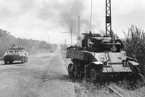 Armored cars of Task Force Howze move past a burning American M3 Stuart light tank that was just knocked out in the push to Rome on 4 June 1944. Several competing task forces wanted to be the first into the Italian capital.
