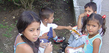Children wait for their parents during the MEDRETE. The gifts given during the civic action have several purposes; the plastic bags at the lower left contain toothpaste, mouthwash and a toothbrush. The packages on the children’s laps have school notebooks, an eraser, ruler, and pencils. 
