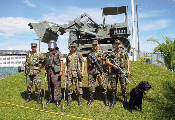 Colombian engineers stationed in Tolemaida display their equipment, including mine detectors, protective equipment, and an explosive-sniffing dog.