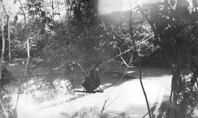 Lancero student commando-crawling across a stream on one-rope bridge.