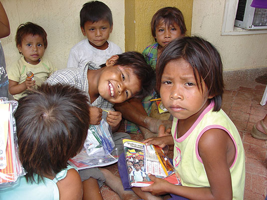 Children wait for their parents during a medical readiness training exercise (MEDRETE) in San José del Guaviare. The gifts given during the civic action have several purposes—the plastic bag in the smiling boy’s hands contain toothpaste, toothbrush, and mouthwash. Both the boy and the girl on the right have a package that has a school notebook, an eraser, ruler, and pencils. The message on the cover of the notebook, “Todos somos Colombia” (We are all Colombia), is part of the government’s information campaign to gain legitimacy.