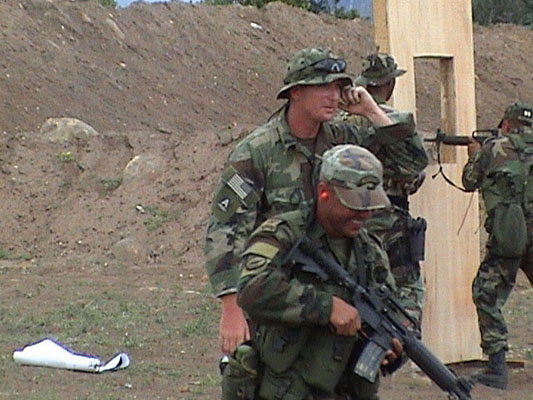 An ODA 746 sergeant takes a BACOA Comando through the shooting course. To their rear another Colombian with an American shoot through a window facade.
