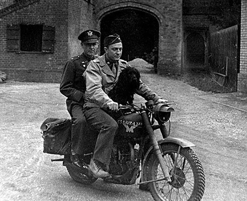 Lieutenant Colonel Chandler takes his bike for a spin. On the back is Major Louis Rafferty and on the front, his pet dog “Ack-Ack.” Ack-Ack was GI slang for “flak” or German antiaircraft fire.