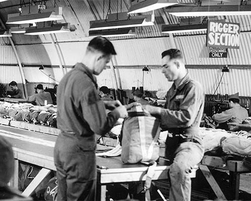Men of the Rigger Section pack parachutes. Notice the bright lighting which helped to ensure that the parachutes were packed correctly.