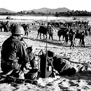 The MARS Task Force, the successor to Merrill’s Marauders, assembles on the banks of a river in Burma. The communications section has established  a radio net to control the operation.