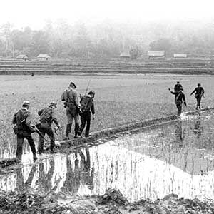 U.S. Special Forces advisors on patrol with their Montagnard team cross a rice paddy dike near Ba To in Quang Ngei Province, South Vietnam in 1963. The Radio-Telephone Operator (RTO) carried the PRC-10, and later PRC-25 and PRC-77 radios to keep contact with the firebase. The use of FM retransmission sites extended the range of the radios.
