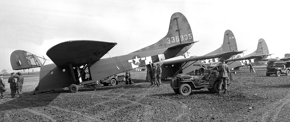 CG-4A “WACO” gliders ready for loading. Notice the pilot’s compartment in the raised nose section and the wooden supports used to elevate the tail to keep the cargo compartment on the ground. This technique made it easier to load bulky supplies and equipment into the glider.