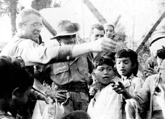 BG Franklin D. Merrill passes out gift to Kachin villagers in mid-March 1944 as Father James Stuart looks on.