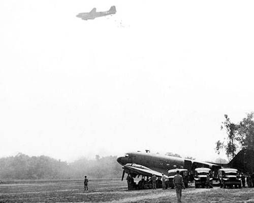A C-47 conducts a free-drop while another has landed for a medical evacuation (ambulances in foreground.)