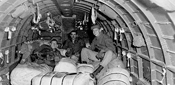 Enlisted men of the Detachment 101 Air Drop Section rest on bundles inside a cargo aircraft.