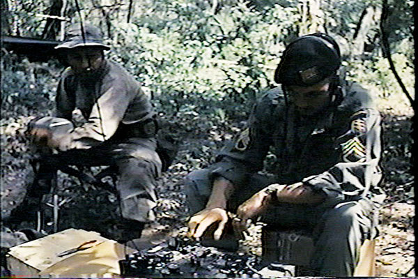SSG William W. Burkett, the Communications Supervisor, sends a Morse Code message using the AN/GRC-109 radio. A Bolivian Ranger is cranking the generator.