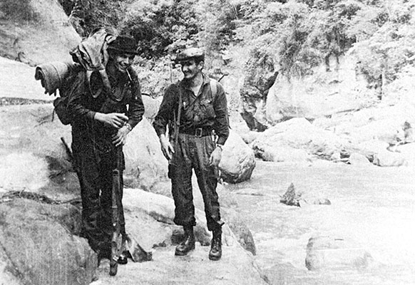 “Miguel,” Cuban Manuel Hernández Osorio, a Sierra Maestra veteran, and “Inti,” Bolivian Guido Peredo Leigue (right), pause after a river crossing during the “Long March.” Notice the  rocky river valley (or canyon) terrain the guerrillas moved over.