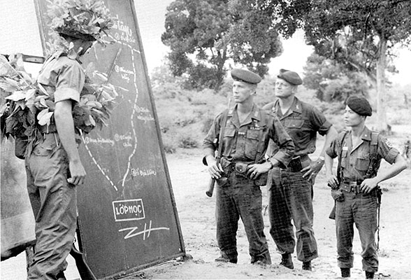 Two U.S. advisors to the Vietnamese Rangers receive an operational briefing from a Vietnamese officer for a live-fire combat tactical exercise at Trung Lap.