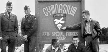Josef and Ctirad “Ray” Masin and Milam Paumer with friends in front of the 77th SFG Gymnasium sign on Smoke Bomb Hill, Fort Bragg, NC.