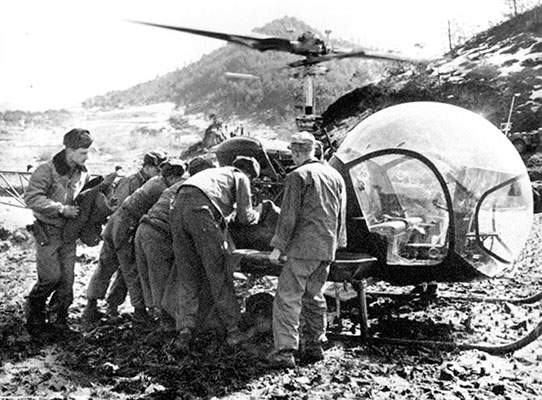 Evacuation of a wounded soldier by H-13 helicopter. CPT Albert C. Sebourn is at far left holding a blanket.