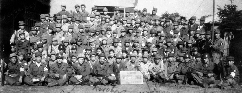 The assembled Ivanhoe Security Force with its American military cadre seated in the front row: 4th from left CPL Joseph Howard, 5th from left SGT Emmett Parker, 7th from left MAJ Jack Young, 9th from left CPL L. Carl Heesch, 12th from left CPL “Moose” Thompson.