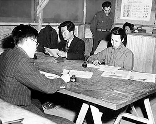 1LT Eddie Deerfield supervises local translators as they prepare broadcast scripts in Korean and Chinese from English copy written by 1st RB&L personnel in Tokyo.