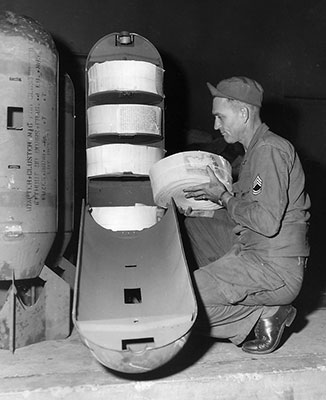 SFC Furl A. Krebs, 3rd Reproduction Company, loads an M11191 cluster bomb adapter with 22,500 (5” X 8”) rolled Psywar leaflets at the FECOM Print Plant. 