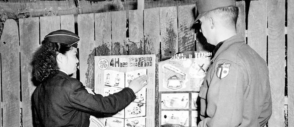 A Civil Assistance soldier and a ROKA female soldier paste KCAC-produced 4-H posters on a fence publicizing a self-help program.