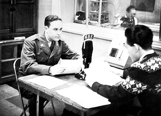During the Army Signal Corps film team visit to the 1st RB&L, PFC Sigmund S. Front discussed an upcoming broadcast script with a Korean announcer in a Radio Tokyo studio of NHK, the Japanese government radio system.