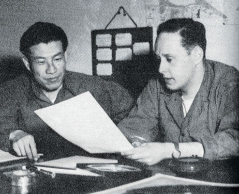 Korean translator Chang Sang Moon listens as the Radio Seoul production man, CPL Sigmund S. “Sig” Front, explains a broadcast.