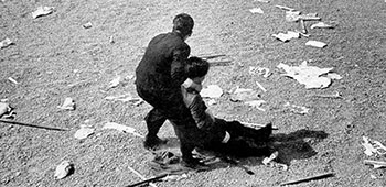 An injured, unconscious policeman is dragged away from the Imperial Plaza cluttered with abandoned bamboo poles, pipes, and placards.