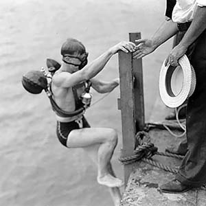 Lambertsen limbing up onto dock after a test of an early rebreather.